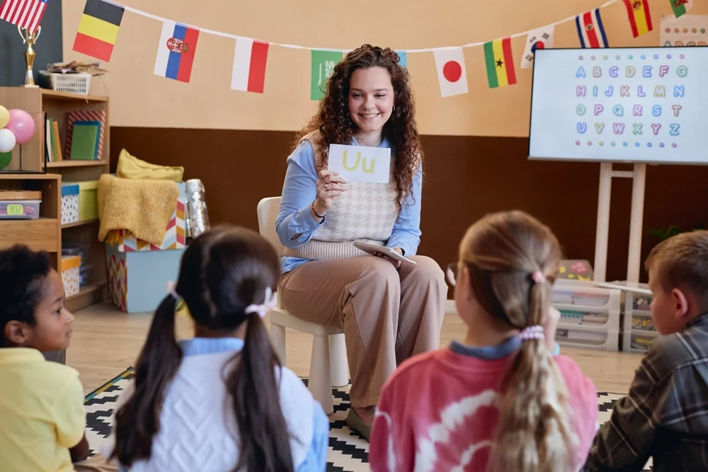 Portrait of smiling female teacher showing alphabet cards to children