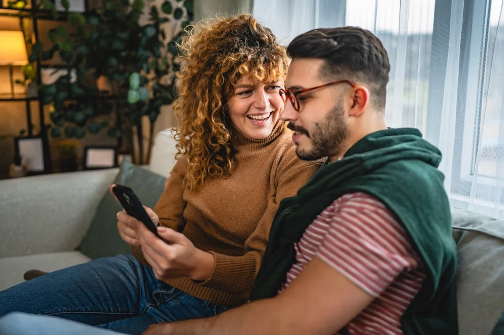 Couple girlfriend and boyfriend having fun while using cellphone on couch