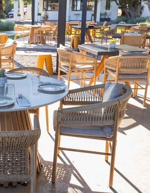 Commercial outdoor restaurant patio with dining tables, woven chairs, and hospitality furniture arranged for guests.