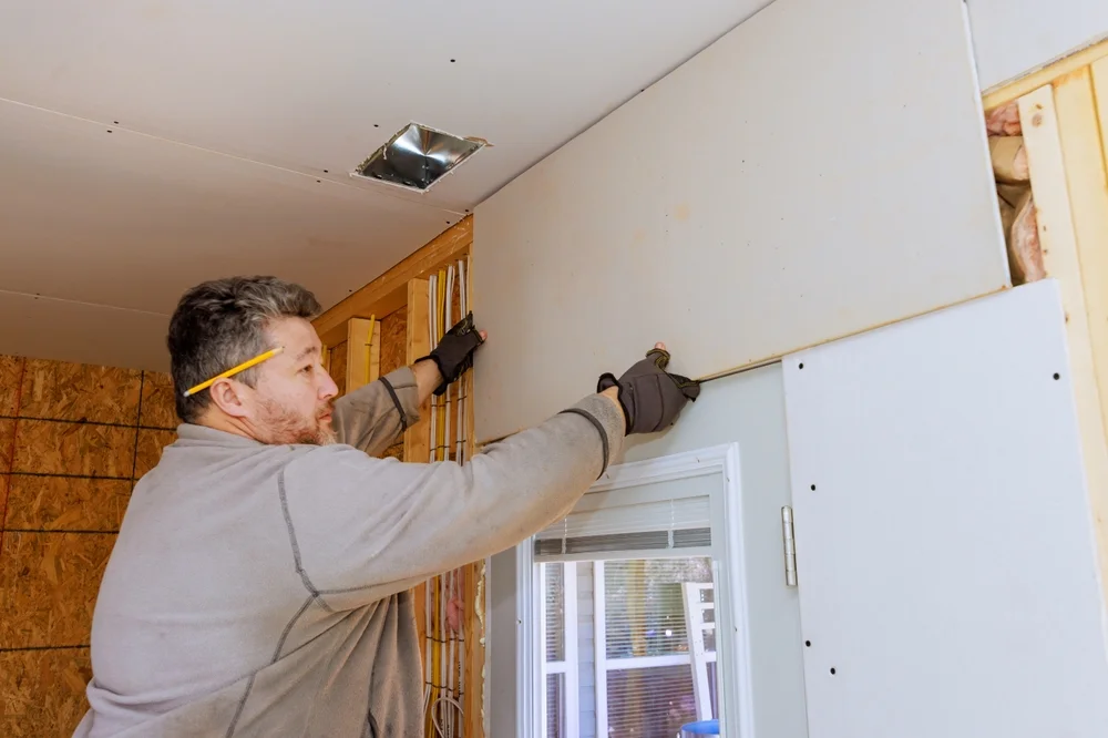 Handyman works on attaching drywall sheetrock to wall in home