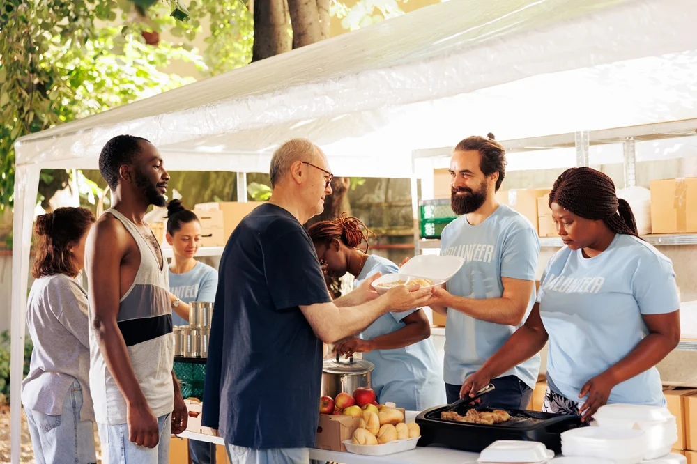 Volunteers serving meals and supporting community members at an outdoor nonprofit event.