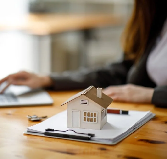 Real estate professional working on a laptop beside a model home, representing property marketing and client management.